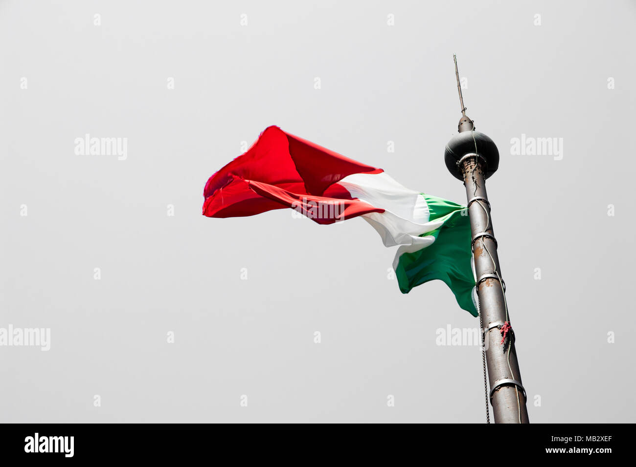 Brandir le drapeau italien colorés dans le vent, et suspendu à un mât avec un fond gris Banque D'Images