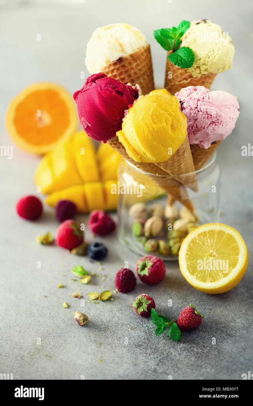 Rouge, rose, jaune, vert, blanc boules de crème glacée dans les cônes alvéolés avec différentes saveurs - mangue, citron vert, menthe, pistache, orange, fraise, Banque D'Images