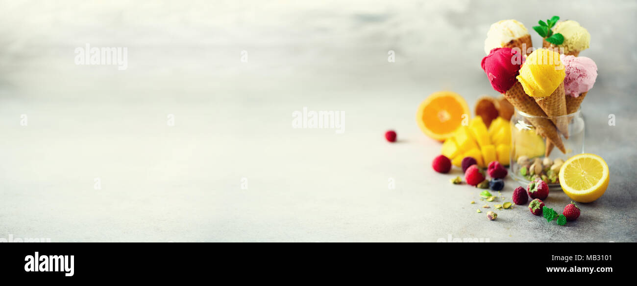 Rouge, rose, jaune, vert, blanc boules de crème glacée dans les cônes alvéolés avec différentes saveurs - mangue, citron vert, menthe, pistache, orange, fraise, Banque D'Images