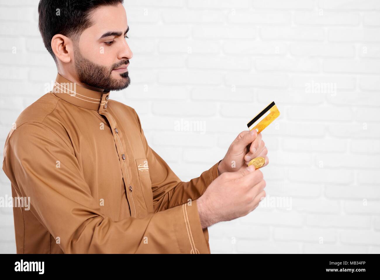 Jeune homme arabe et bitcoin permet de carte de crédit en or sur le fond blanc. Il intéressant d'usure l'usure d'arabie avec un motif précis. Un homme a l'air très occupé, il doit prendre une décision importante. Banque D'Images