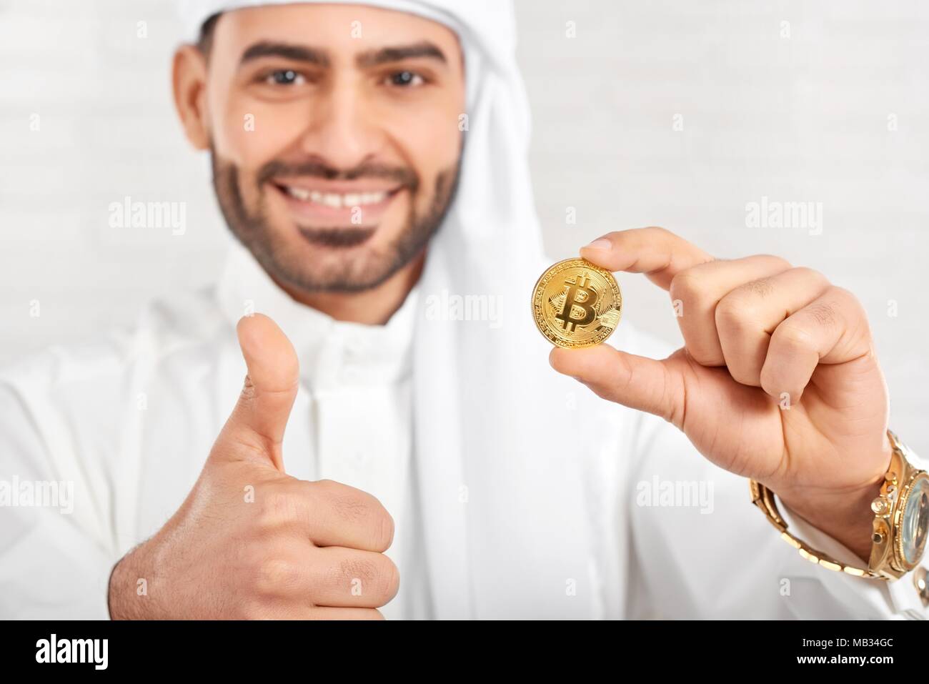 Studio Portrait of a smiling woman arabe et bitcoin permet a l'air très heureux, debout sur fond blanc. Il porte le costume traditionnel arabe blanc,golden watch et les boutons de manchette. Banque D'Images