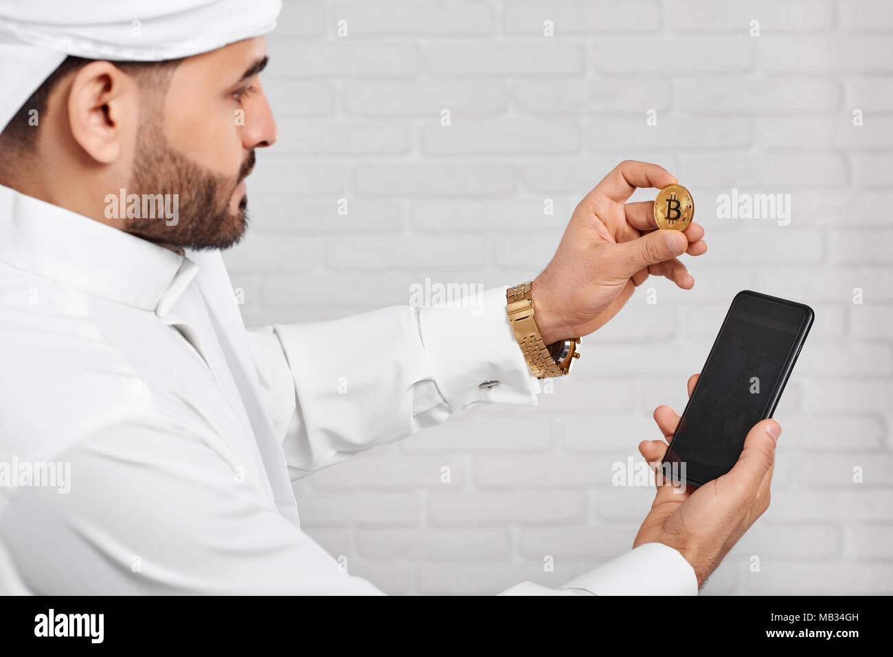Arabian woman blanc traditionnel de maintien de l'usure musulmane bitcoin d'or et le téléphone mobile. Il a golden watch sur la main gauche. Un homme a l'air très occupé Banque D'Images