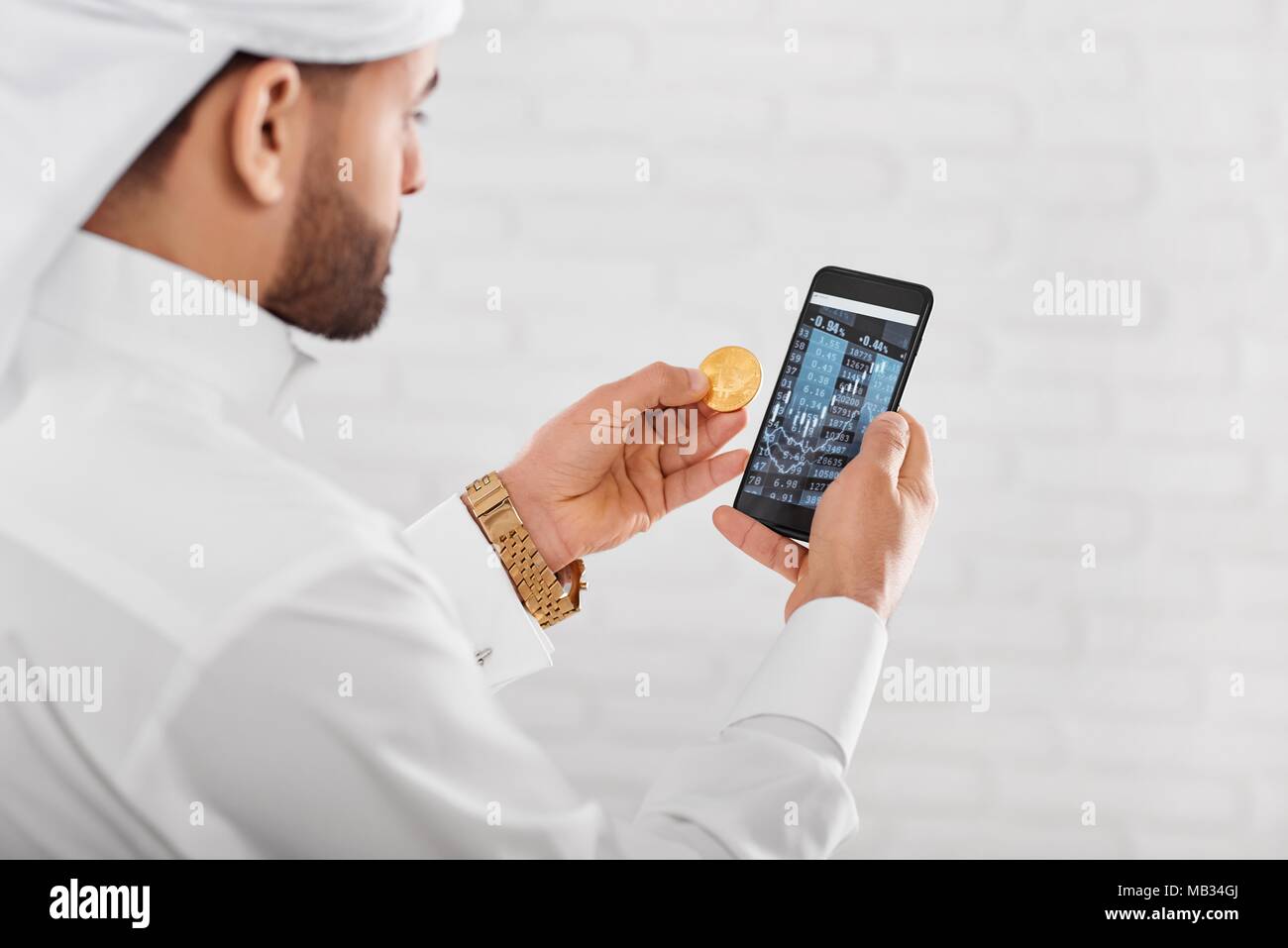 Dans cryptotrader musulmane arabe traditionnel blanc porter des keepins bitcoin or et téléphone mobile. Il a golden watch sur la main gauche. Un homme a l'air très occupé Banque D'Images
