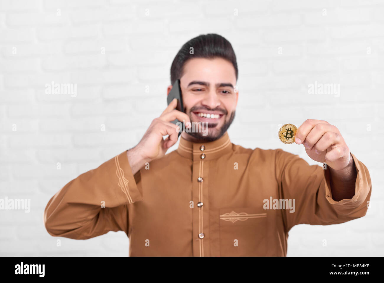 Smiling businessman arabe golden garde. bitcoin En même temps il parle sur son téléphone mobile. Homme porte une chemise marron avec un motif. Close-up a été faite sur le fond blanc. Banque D'Images