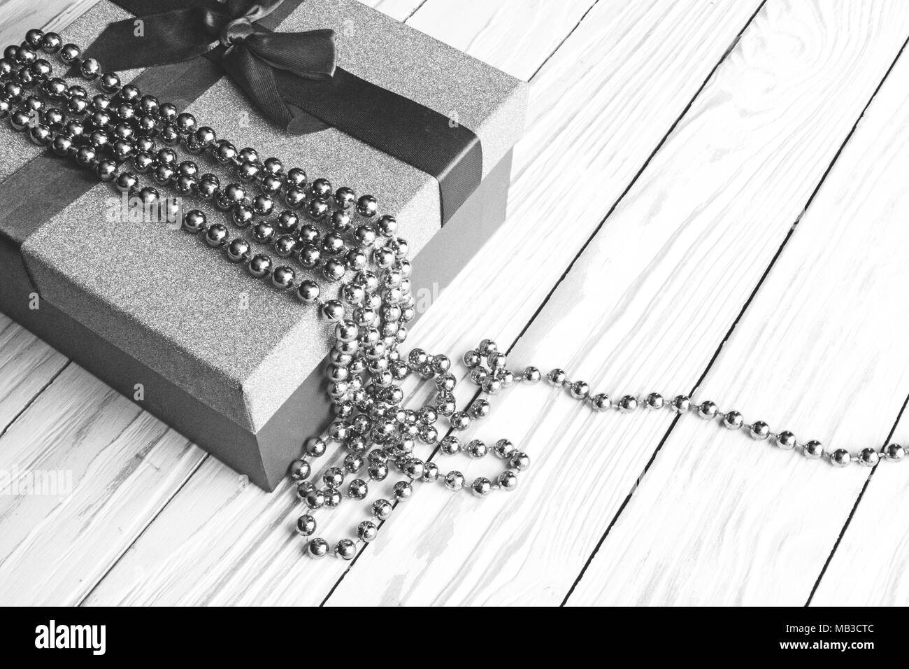 Boîte-cadeau avec du ruban et des perles sur fond de bois, noir et blanc photo gros plan. Banque D'Images