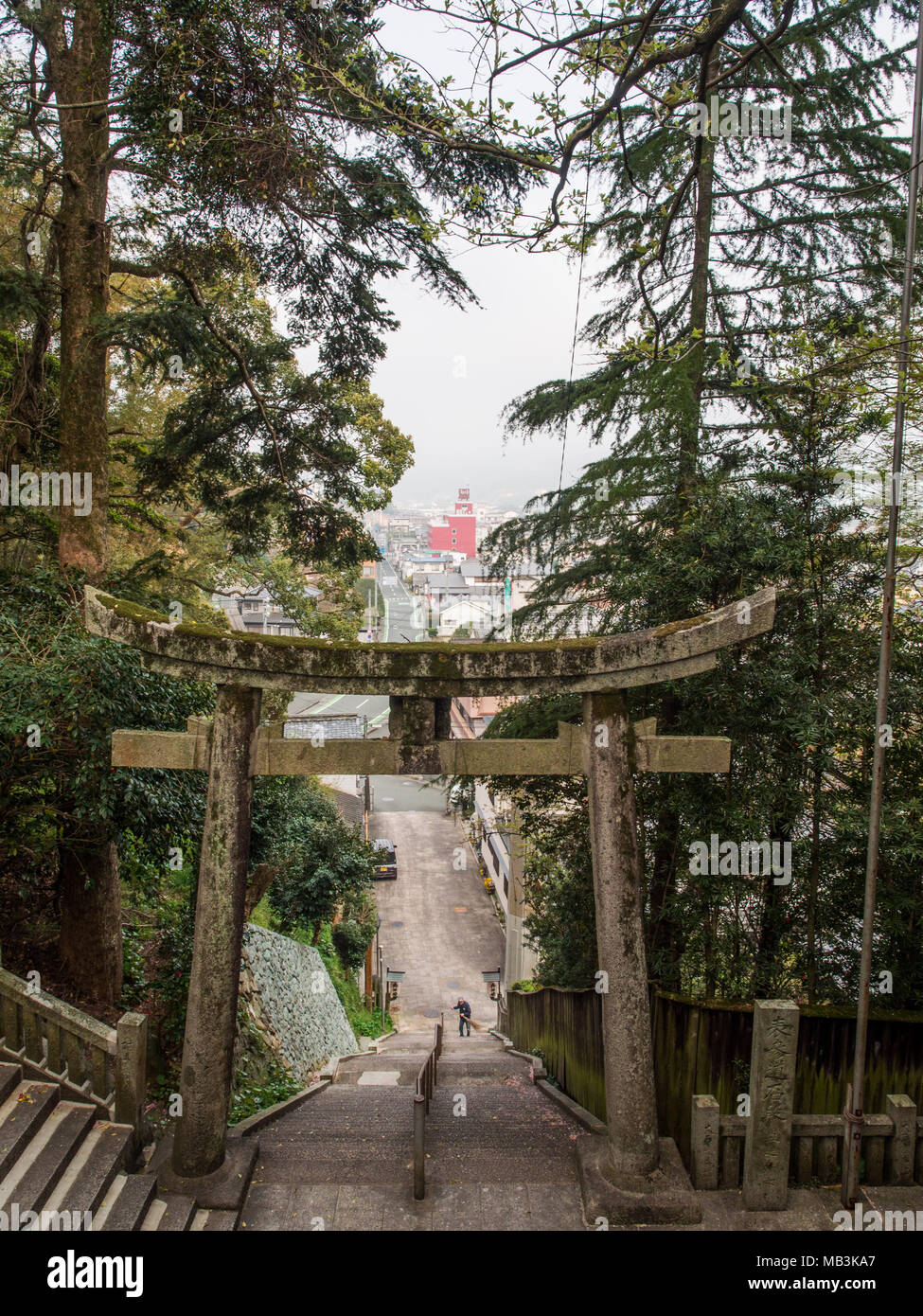 Torii et étapes menant à Ozu de culte, Ozu, Ehime, Shikoku, au Japon. Un homme balaie les escaliers, la ville d'Ozu peut être vu au-delà. Banque D'Images