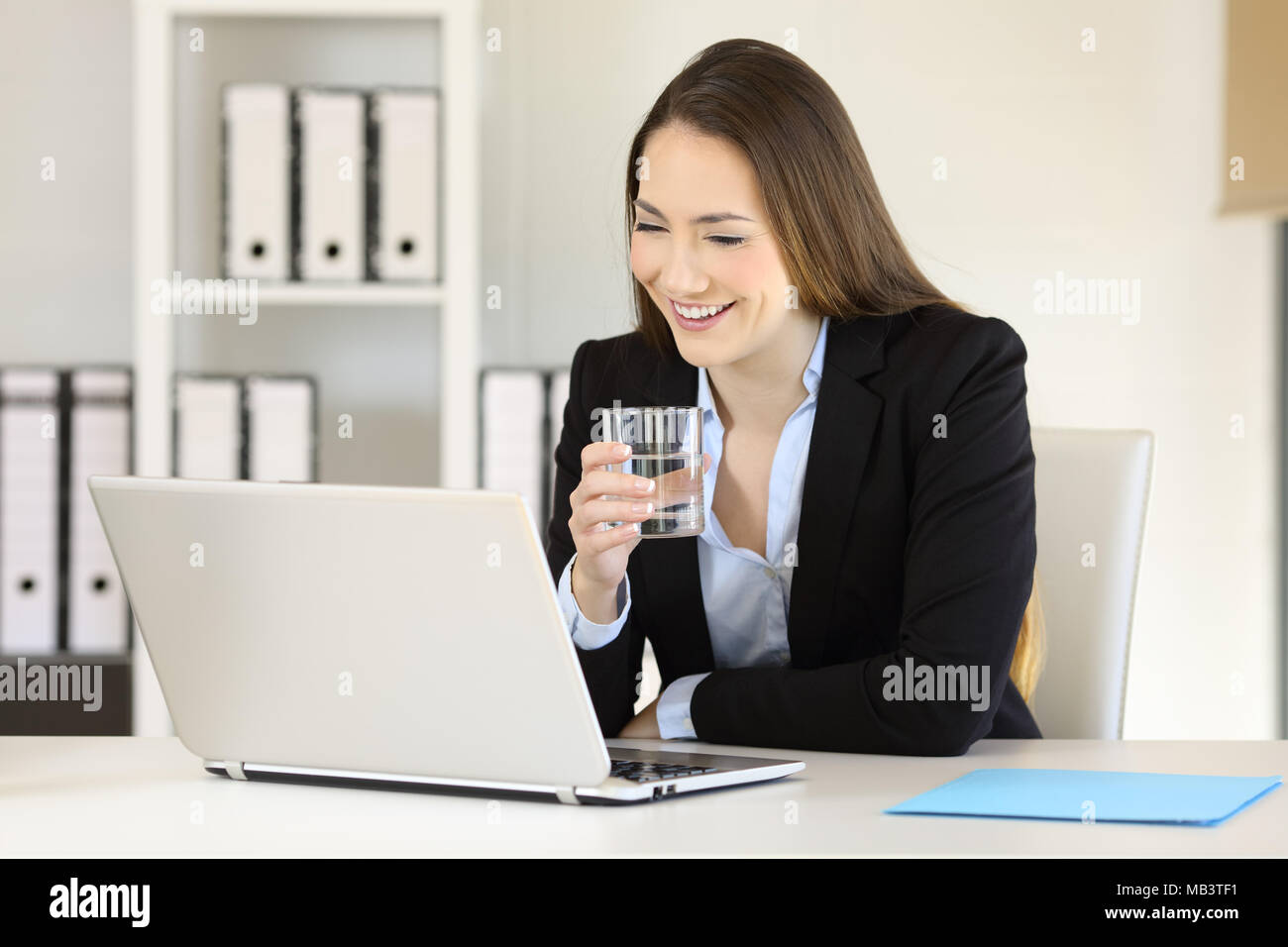 Travail de bureau tenant un verre d'eau sur la ligne de lecture de contenu dans un ordinateur portable Banque D'Images
