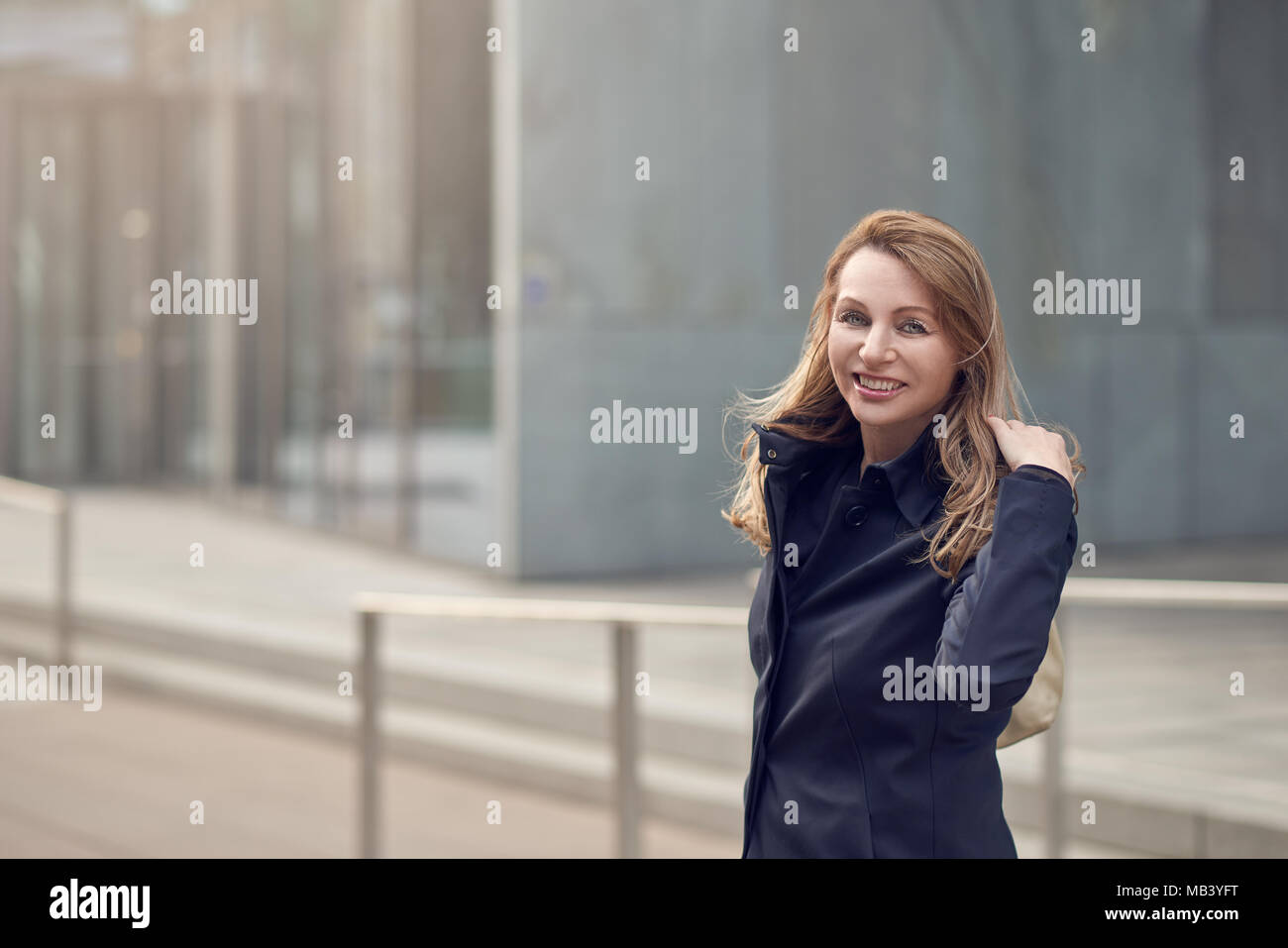 Happy smiling woman standing dans le vent sur une rue urbaine avec ses longs cheveux autour de son visage avec copie espace latéral Banque D'Images
