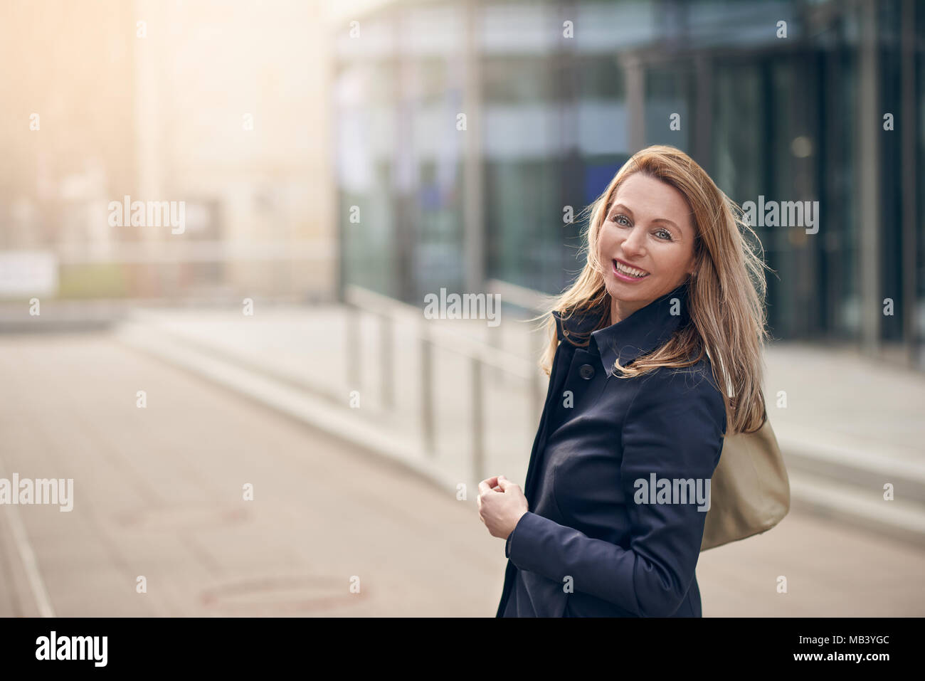 Happy smiling woman standing dans le vent sur une rue urbaine avec ses longs cheveux autour de son visage avec copie espace latéral Banque D'Images