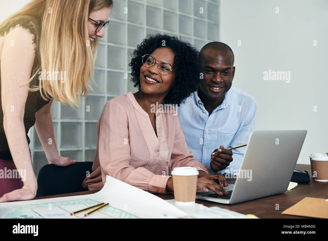 Groupe de divers collègues de sourire et d'avoir une discussion sur un ordinateur portable tout en travaillant ensemble à un bureau dans un bureau moderne Banque D'Images
