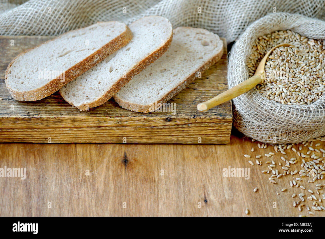 Sur une planche en bois se trouvent les tranches de pain. A proximité se trouve un sac de blé. La récolte de céréales d'automne. Banque D'Images