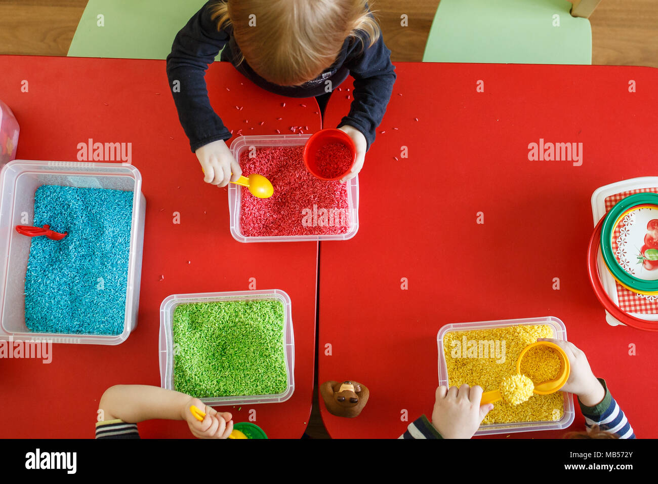 Les tout-petits à jouer avec boîte sensorielle avec riz coloré en rouge sur le tableau. Vue d'en haut. Banque D'Images