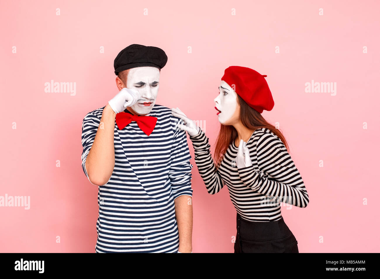 Cri de l'homme, sa femme calme et essuie les larmes. Clown, artiste , pantomime . Fond rose, Studio shot Banque D'Images