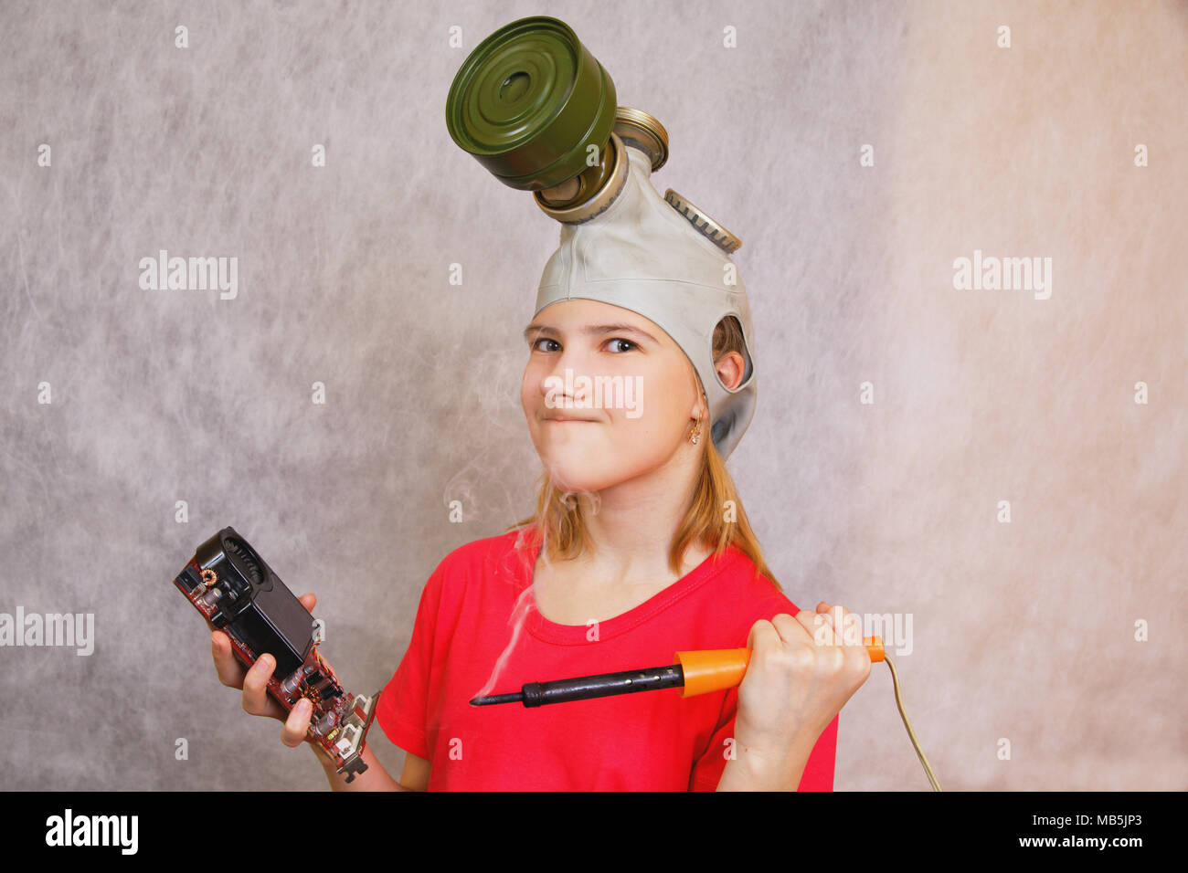 Comic, distorsion : adolescent fille portant un masque à gaz, se prépare à Pierce, détruire un fer à souder chaud non-travail carte électronique Banque D'Images