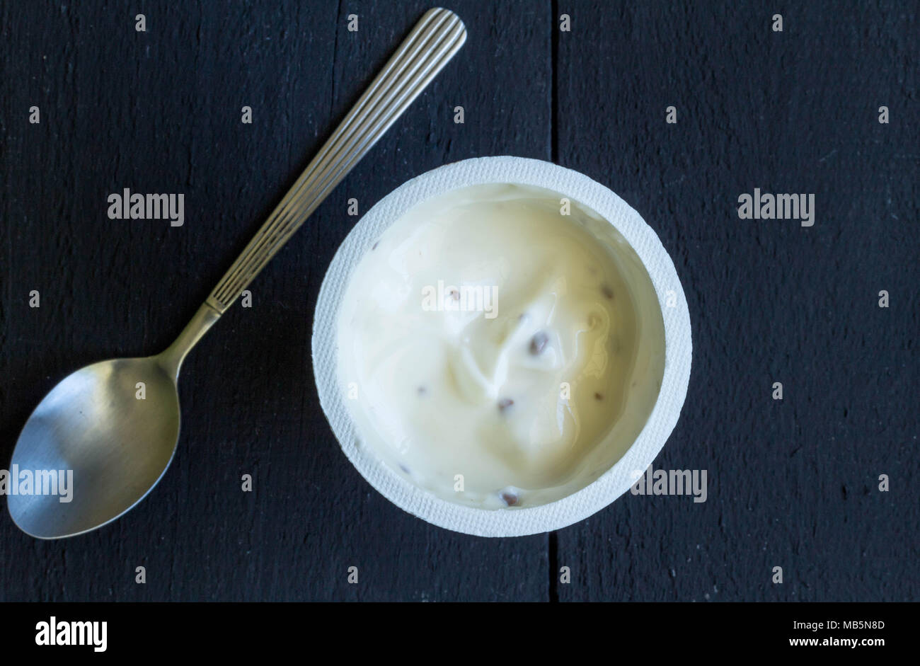 Le yogourt dans tasse en plastique close up sur le tableau noir. Haut Voir photo de vanille Choc Chip yaourt avec cuillère en argent Banque D'Images