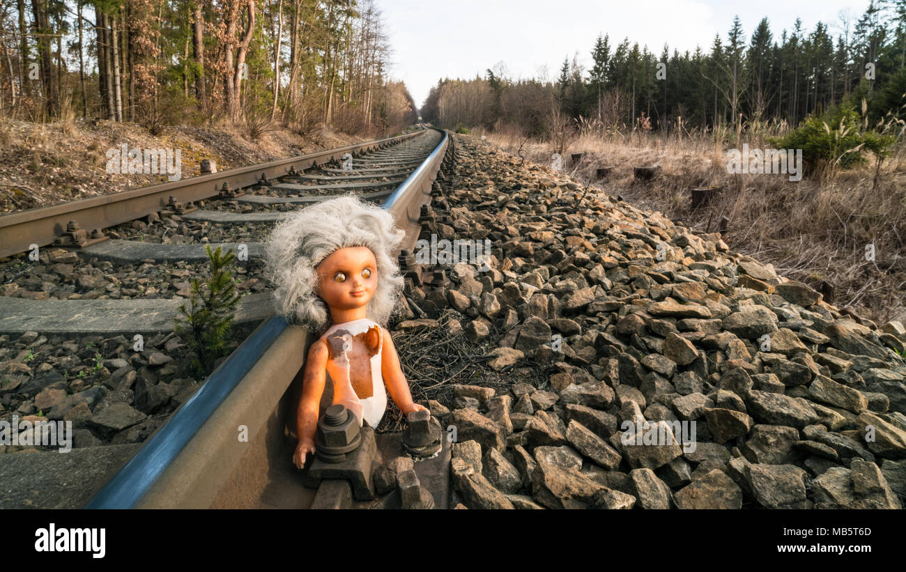 Poupée cassée sur rail train dans la ville ensoleillée de paysages forestiers. Jouet d'enfant perdu à l'ancienne voie de chemin de fer rouillé. Danger, de l'enfance, le devenir, d'accident, sci-fi, de la guerre, de l'abus. Banque D'Images