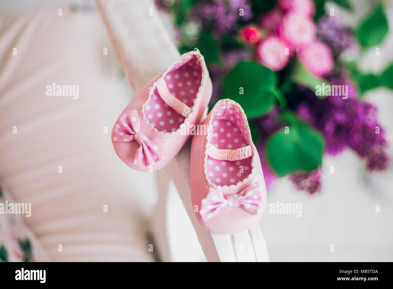 Libre Vue de dessus de paire de petites patates nouvelles chaussures rose pour petit enfant sur le canapé dans votre intérieur. Fleurs colorées floues en arrière-plan. Professionnels s'attendent à ce que Banque D'Images