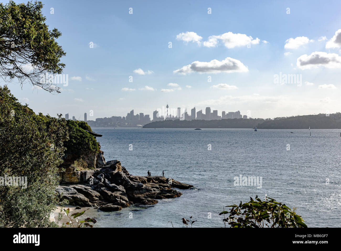 Les hommes de la pêche sur les rochers à Lady Bay Beach avec le Sydney skyline en arrière-plan Banque D'Images