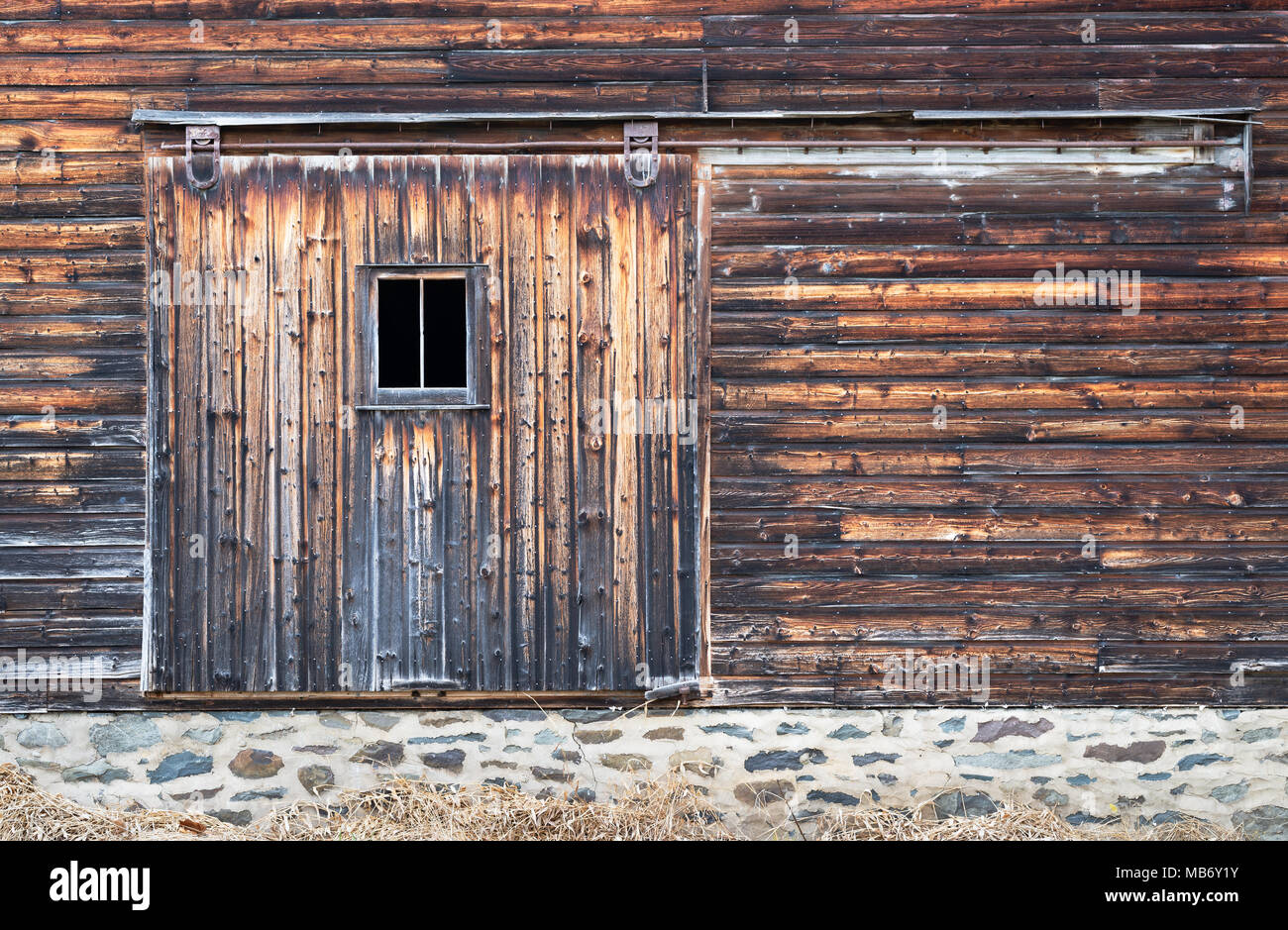 Côté de Barn montrant Distressed Board porte avec fenêtre et mur de pierre Foundation. Banque D'Images