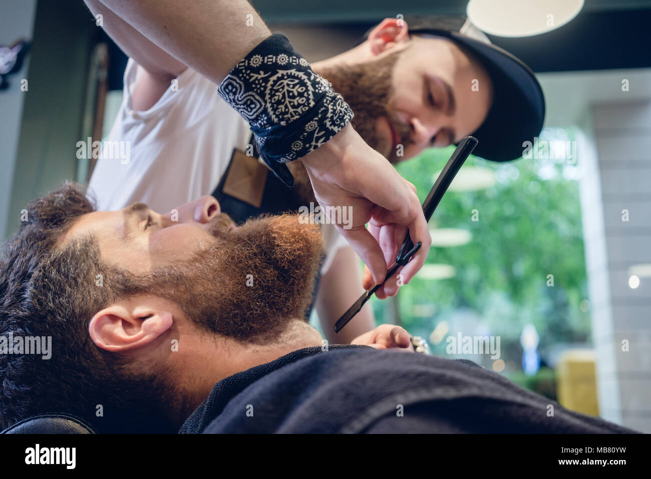 Jeune homme barbu prêt pour le rasage dans le salon de coiffure d'une main-d'coiffure Banque D'Images