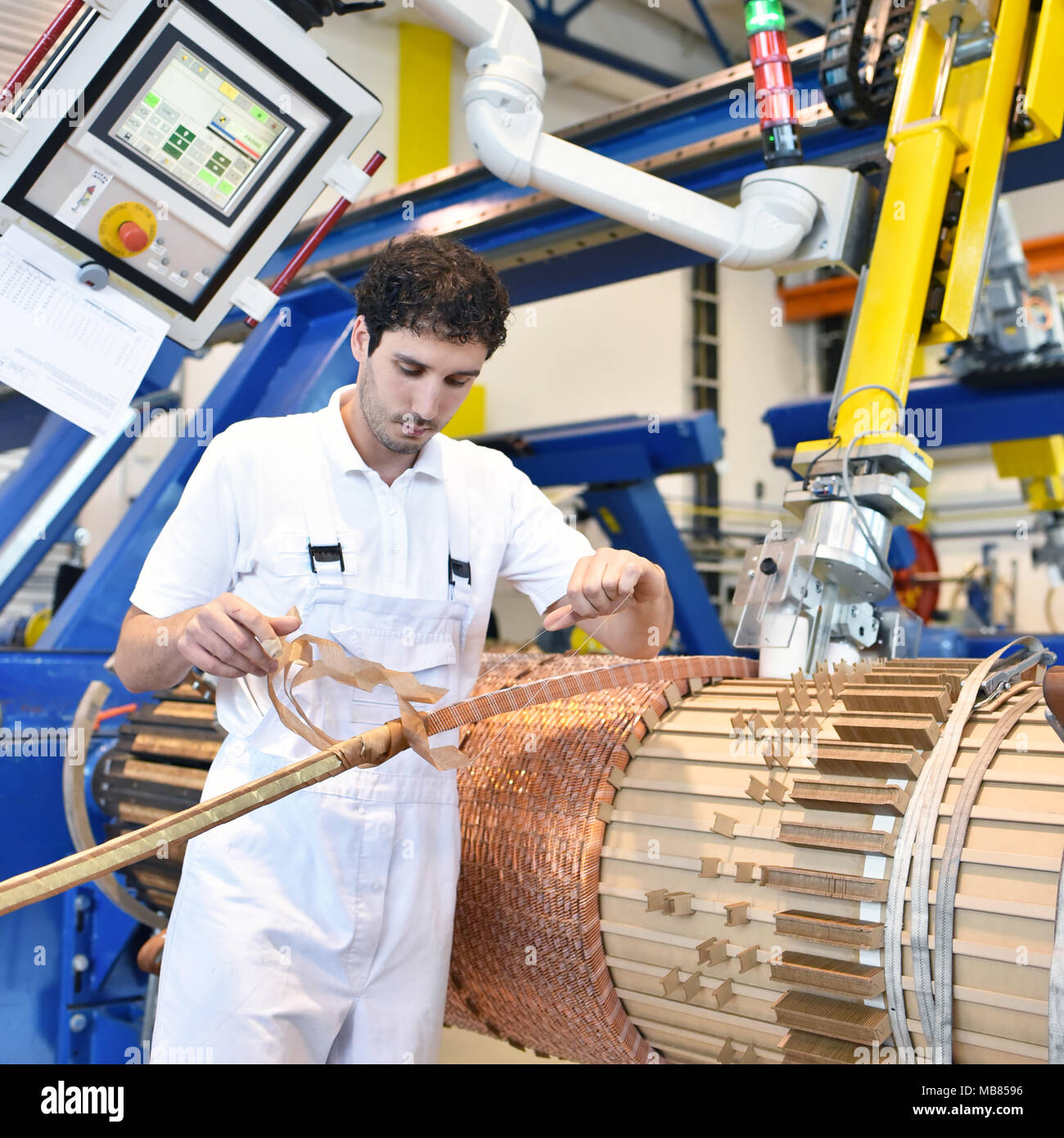 Les jeunes travailleurs de l'ingénierie mécanique l'exploitation d'une machine pour enrouler le fil de cuivre - fabrication de transformateurs dans une usine Banque D'Images