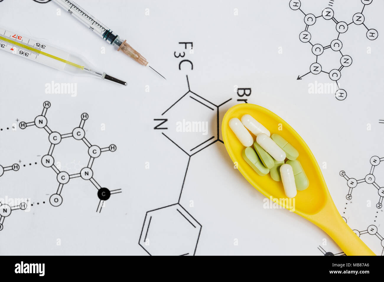 Assortiment de comprimés et gélules en jaune une cuillère, seringue, thermomètre sur fond blanc avec des formules chimiques. Banque D'Images