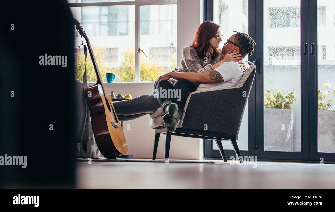 Couple passionné sur un fauteuil dans la salle de séjour. Femme assise sur les genoux de son petit ami et à la recherche à l'autre. Banque D'Images