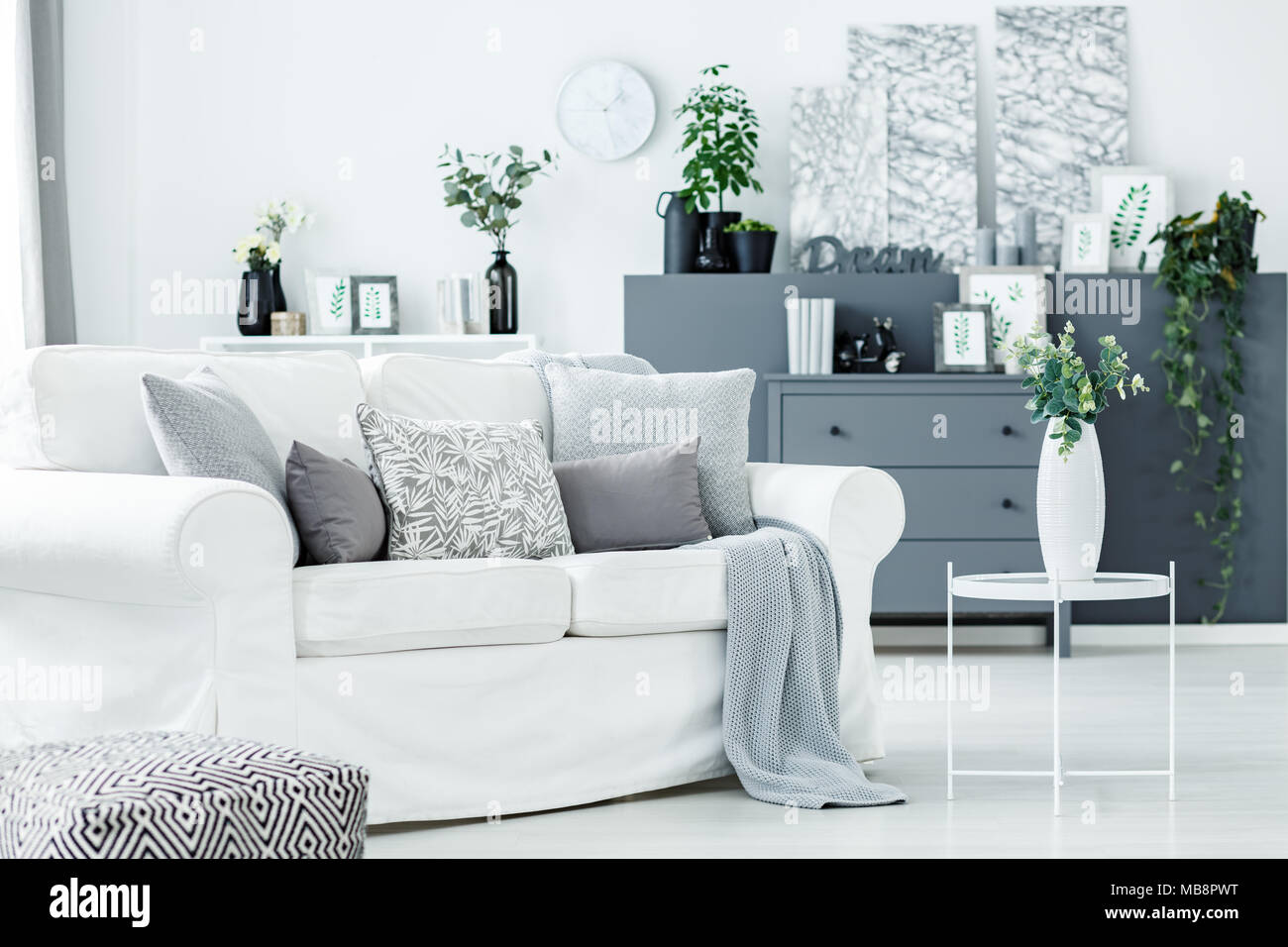 Dans un espace de détente confortable salon monochromatiques avec des plantes d'intérieur, gris et blanc commode canapé Banque D'Images