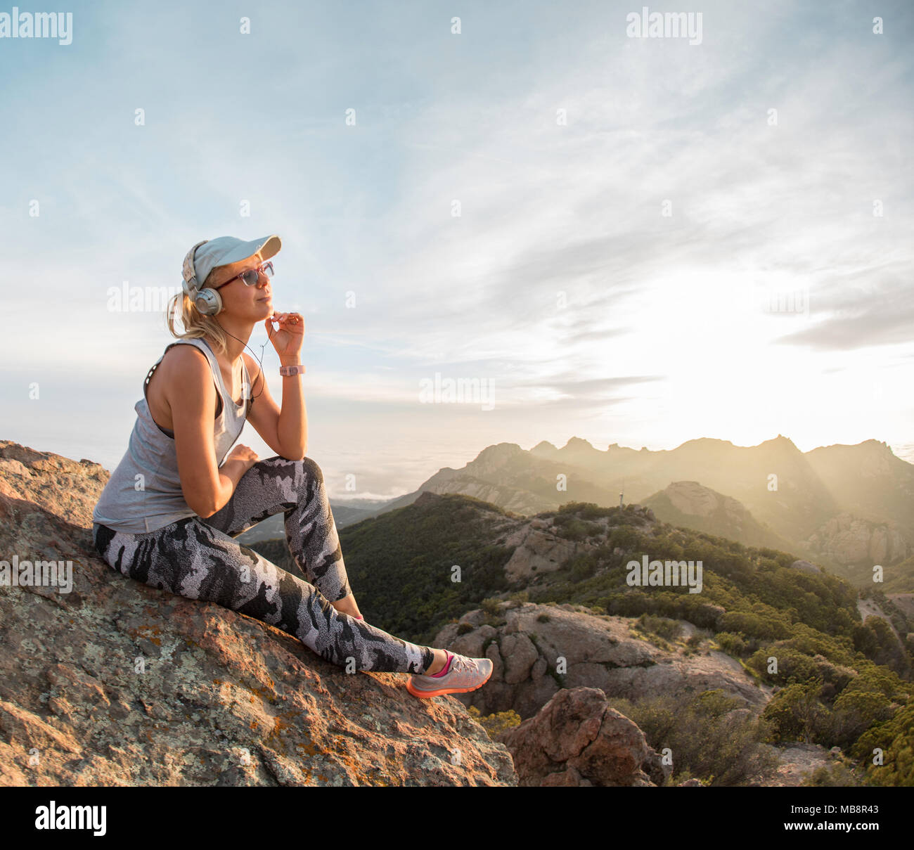 Pensive young girl in headphones bénéficiant beau coucher du soleil sur le sommet d'une montagne Banque D'Images