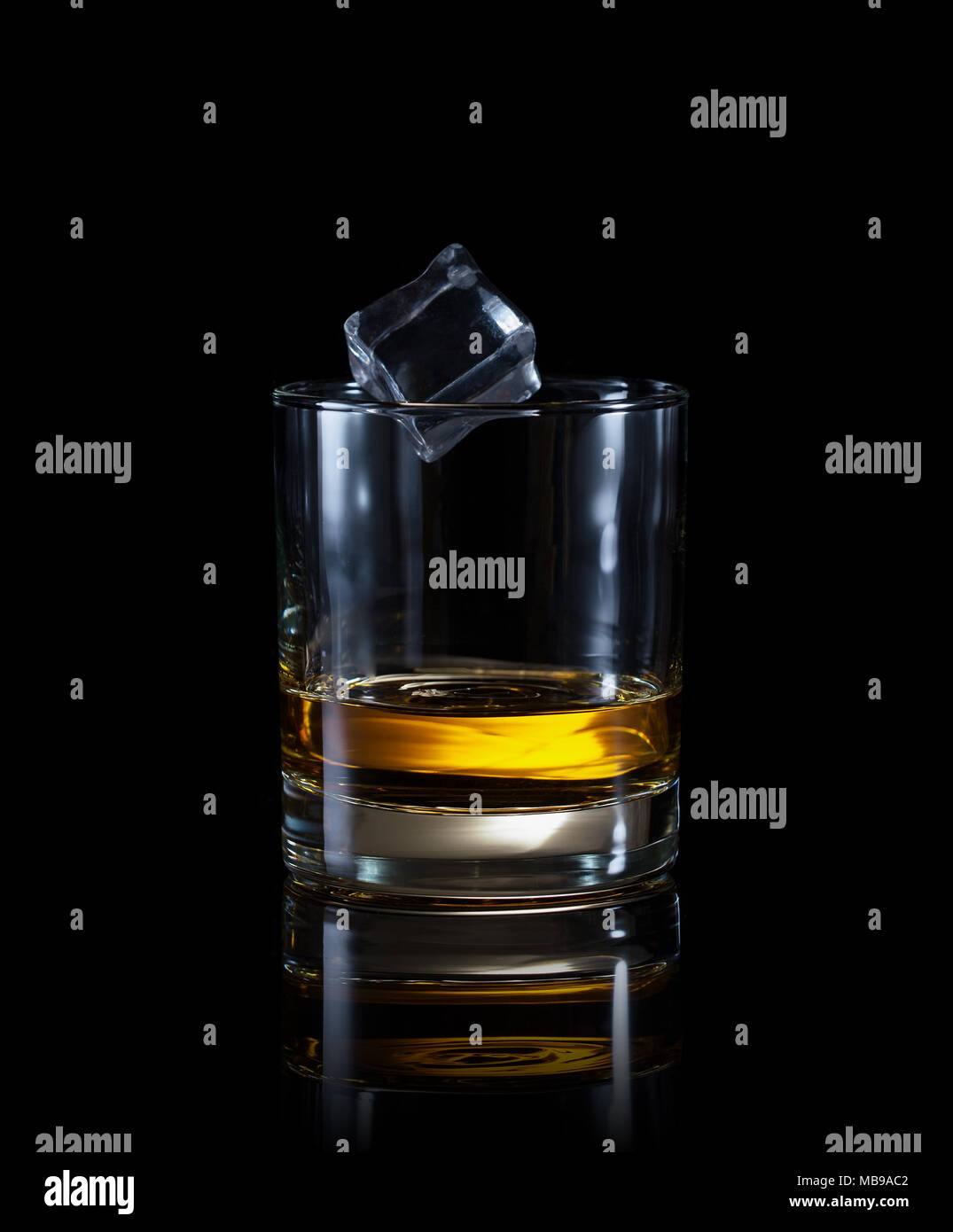 Verre de whisky avec flying ice cube isolé sur un fond noir Banque D'Images