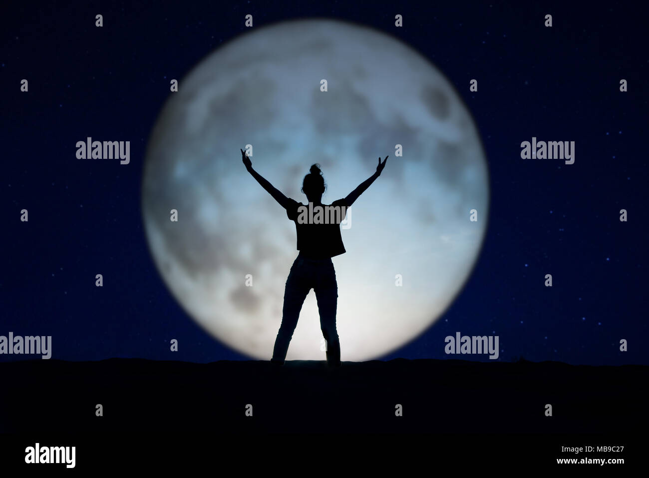 Silhouette d'une femme debout dans la nuit avec les bras vers le haut, giant lune en arrière-plan Banque D'Images