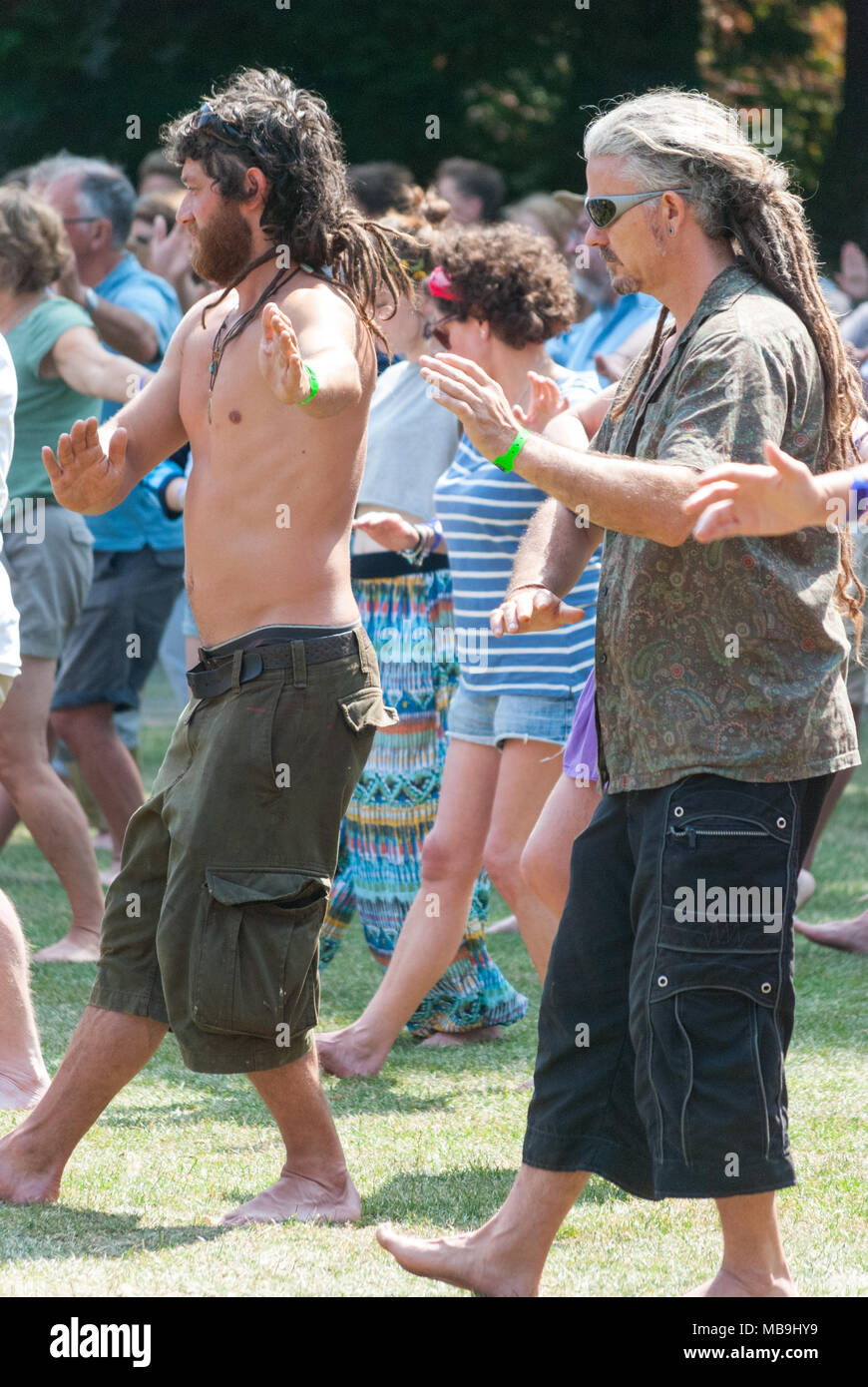 Les gens qui fréquentent une classe de yoga en plein air à un festival de musique. Les hommes aux cheveux longs en dreadlocks. Banque D'Images