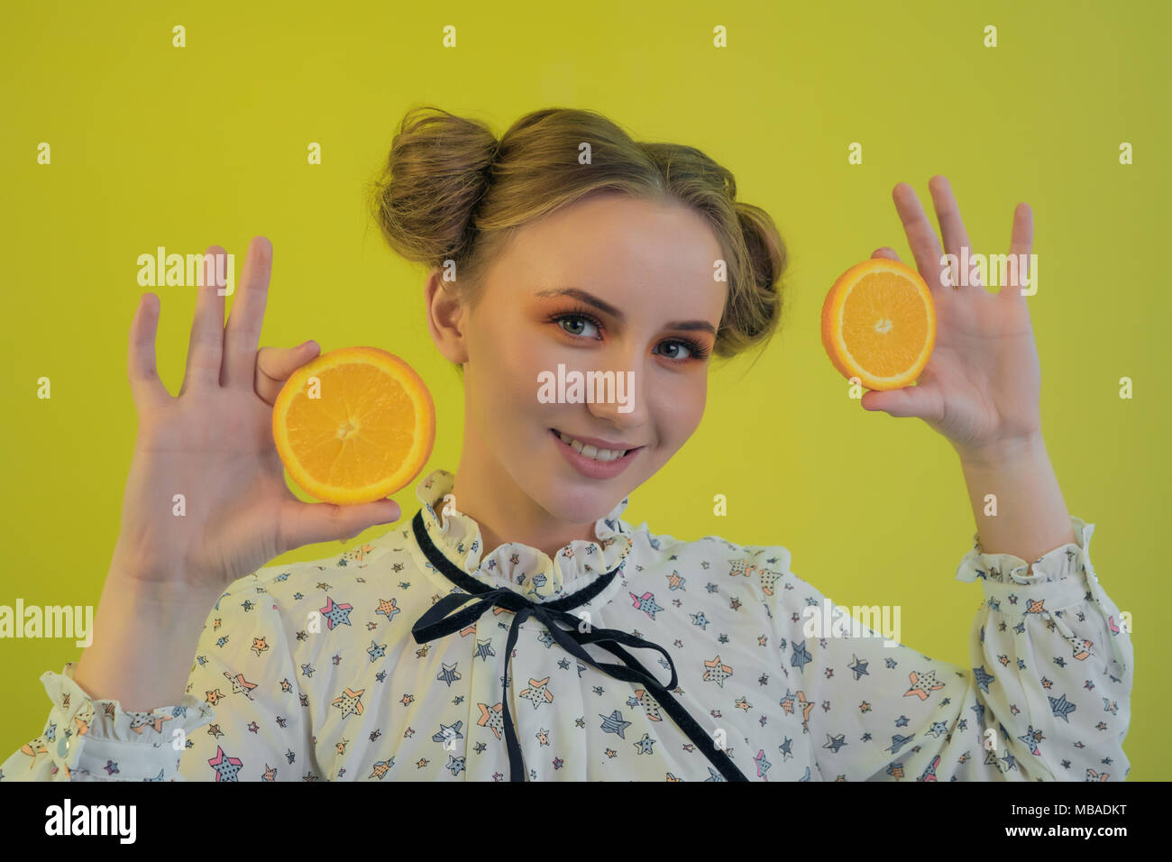 Belle jeune fille drôle holding tranches de oranges dans les mains sur fond lumineux Banque D'Images