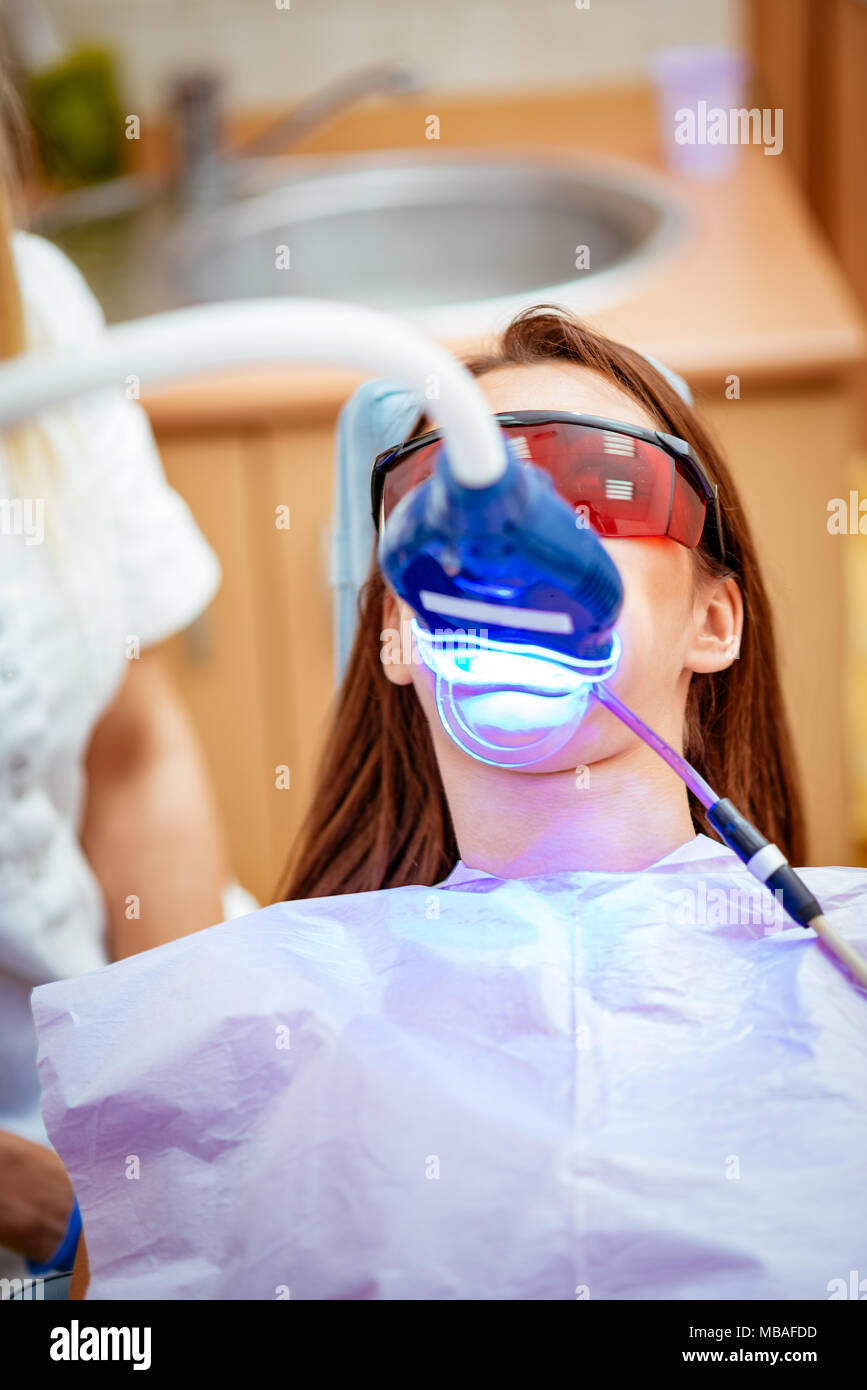 Belle jeune femme en visite au bureau de dentiste, blanchiment des dents avec la lumière ultraviolette. Banque D'Images