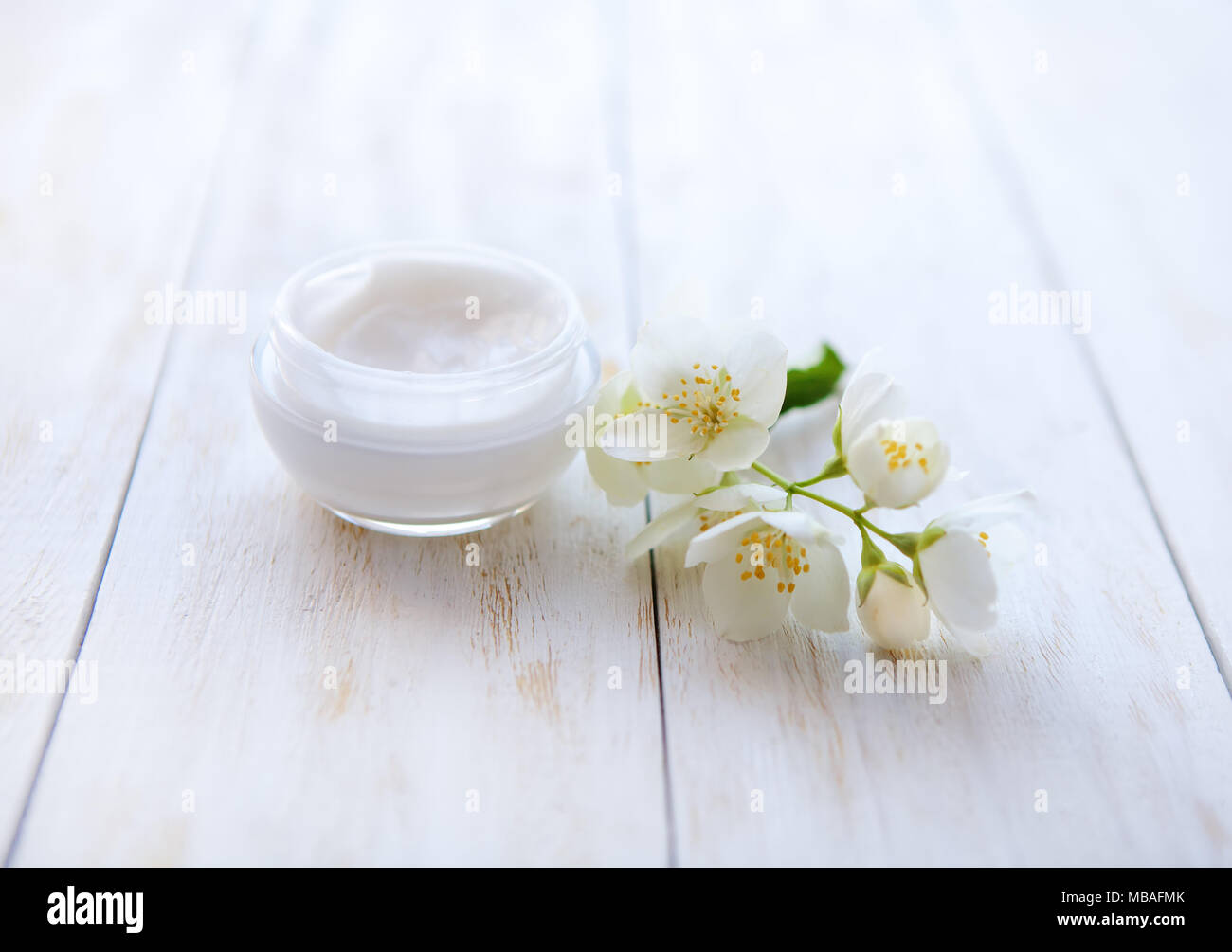 Pot de crème de beauté entouré de fleurs de jasmin sur table en bois blanc Banque D'Images