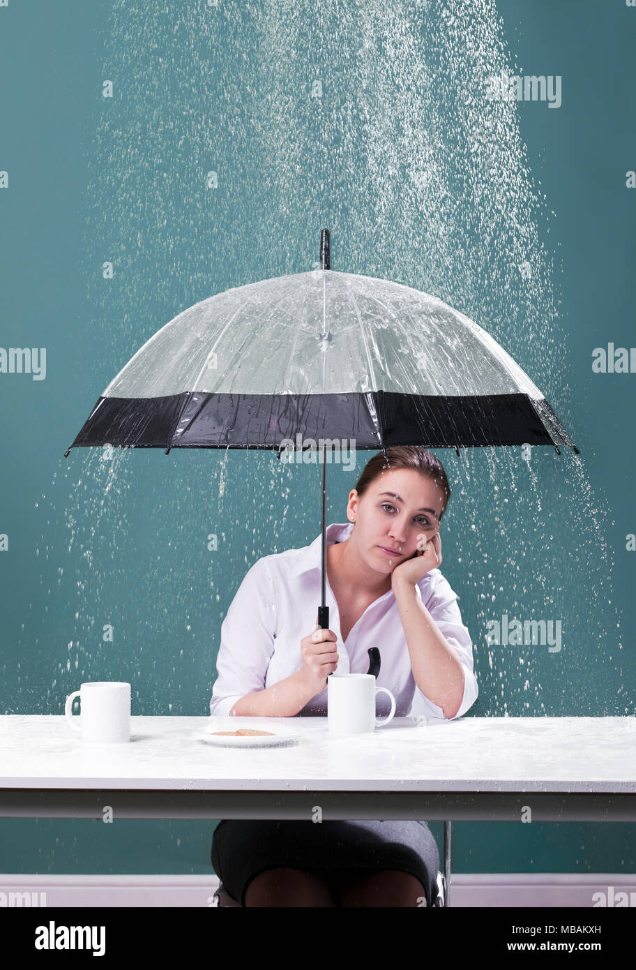 Femme assise à une table avec parapluie sous la pluie Banque D'Images