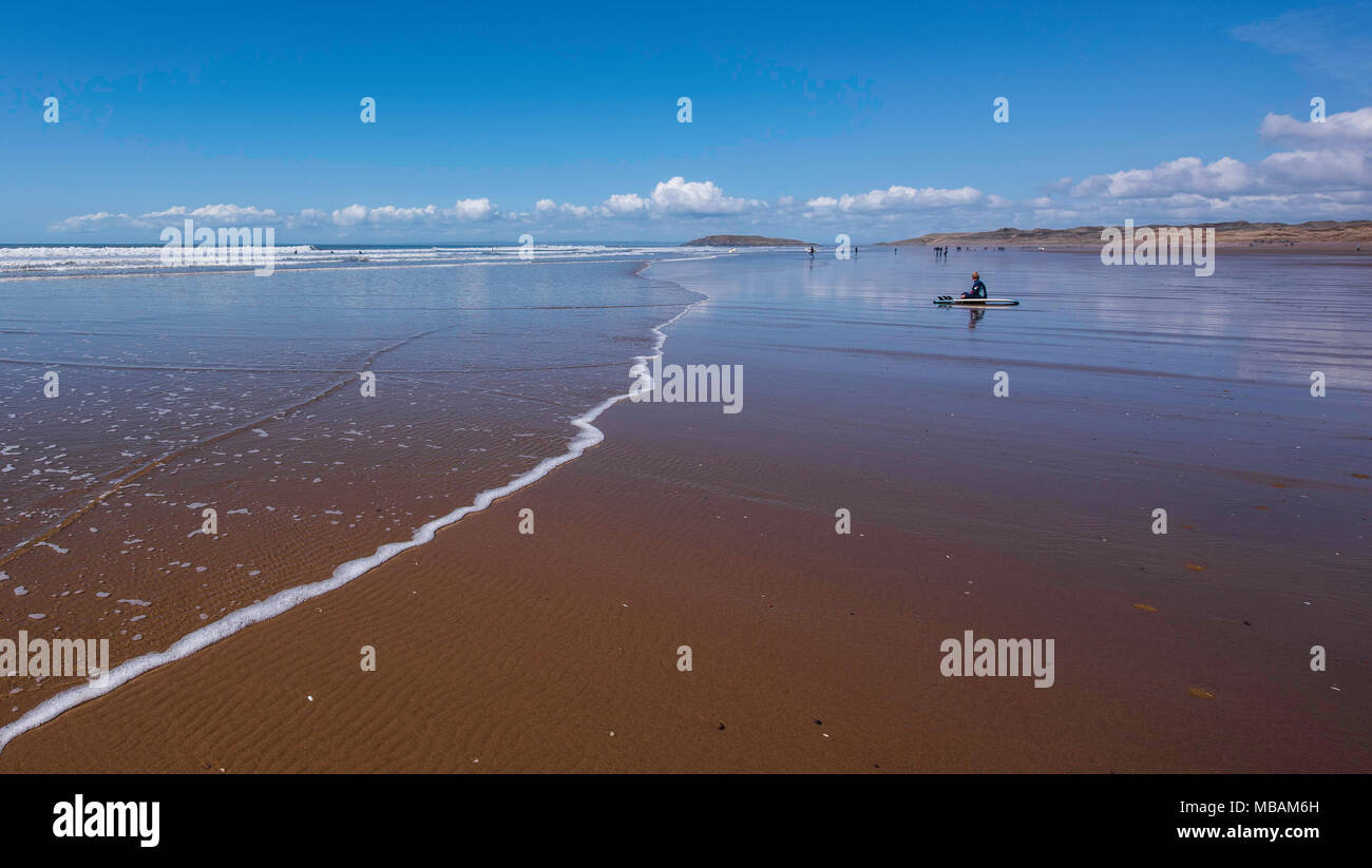 Un surfboarder reste sur la plage de Rhossili Bay, Gower, dans le sud du Pays de Galles, Royaume-Uni. Banque D'Images