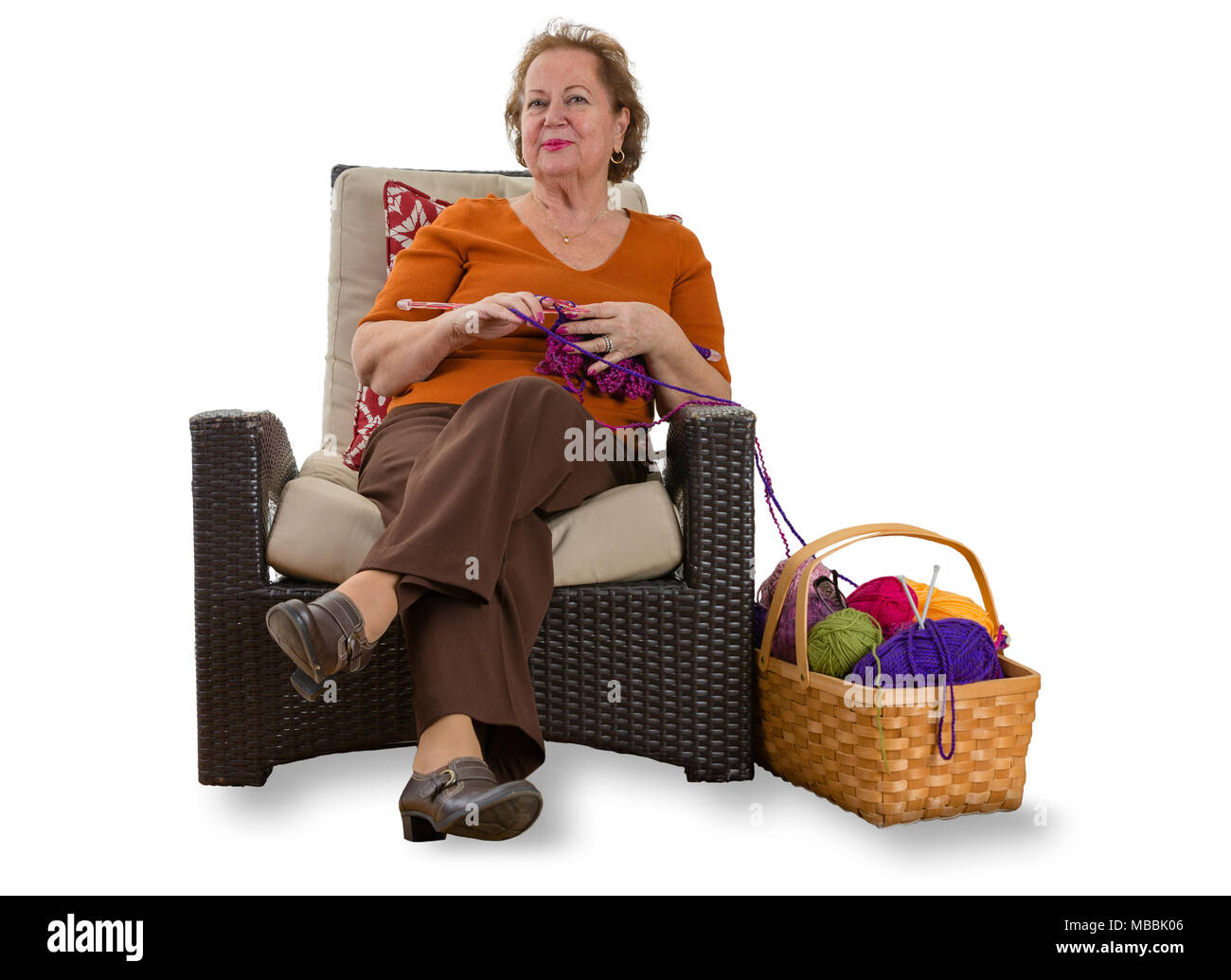Dame âgée heureux de vous détendre dans un fauteuil en osier avec son tricot et un panier de balles colorées de laine à ses côtés sur fond blanc avec l'exemplaire s Banque D'Images