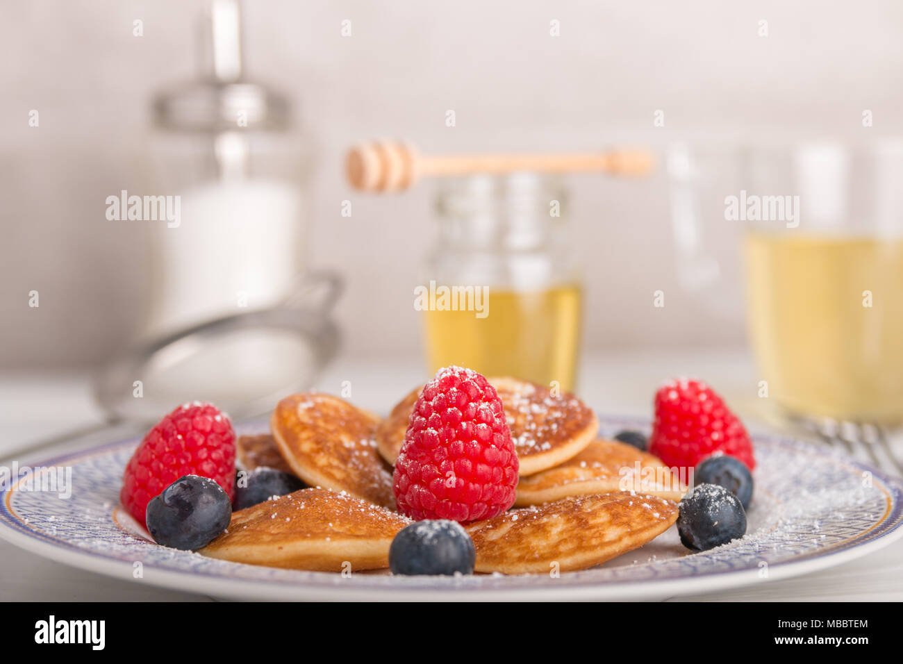 Mini crêpes avec des fruits et du miel sur un plateau avec du thé et du miel dans l'arrière-plan Banque D'Images