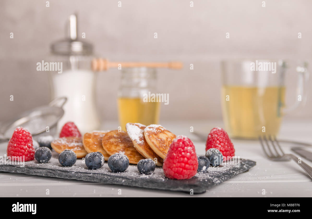 Mini crêpes avec des fruits et du miel sur un plateau avec du thé et du miel dans l'arrière-plan Banque D'Images