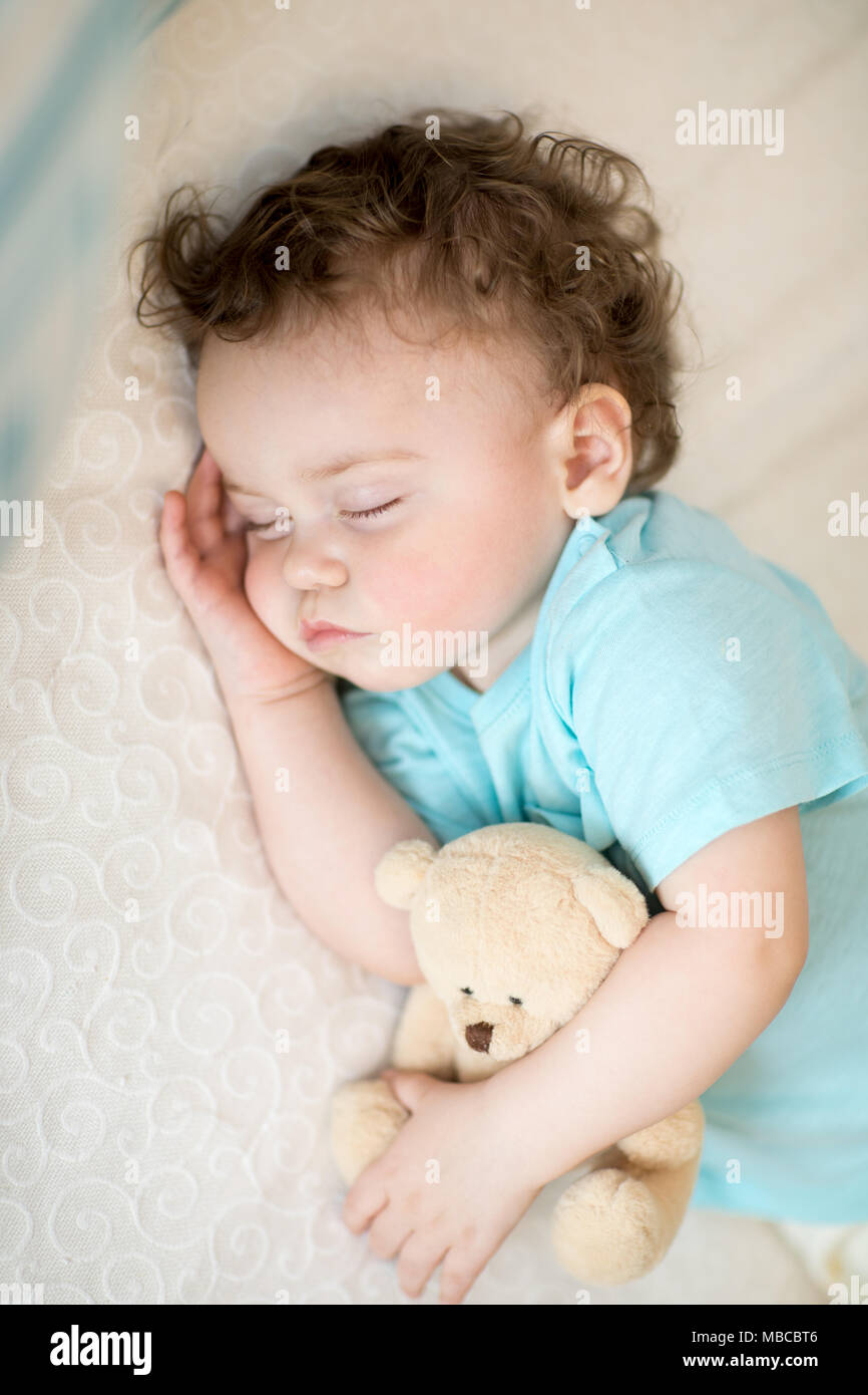 Enfant endormi dans le lit, tenant un ours en peluche. Banque D'Images
