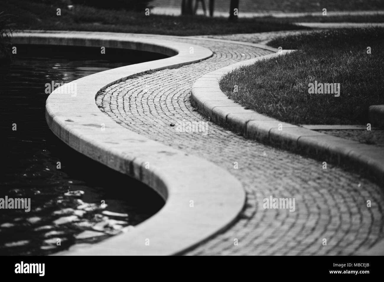 Un trottoir de brique en courbe à côté d'une pièce d'eau dans un parc à Brno, République tchèque. Banque D'Images