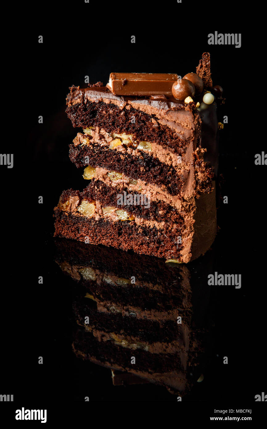 Morceau de gâteau au chocolat savoureux avec couche crémeuse au chocolat décoré entre bonbons servis sur fond miroir noir Banque D'Images