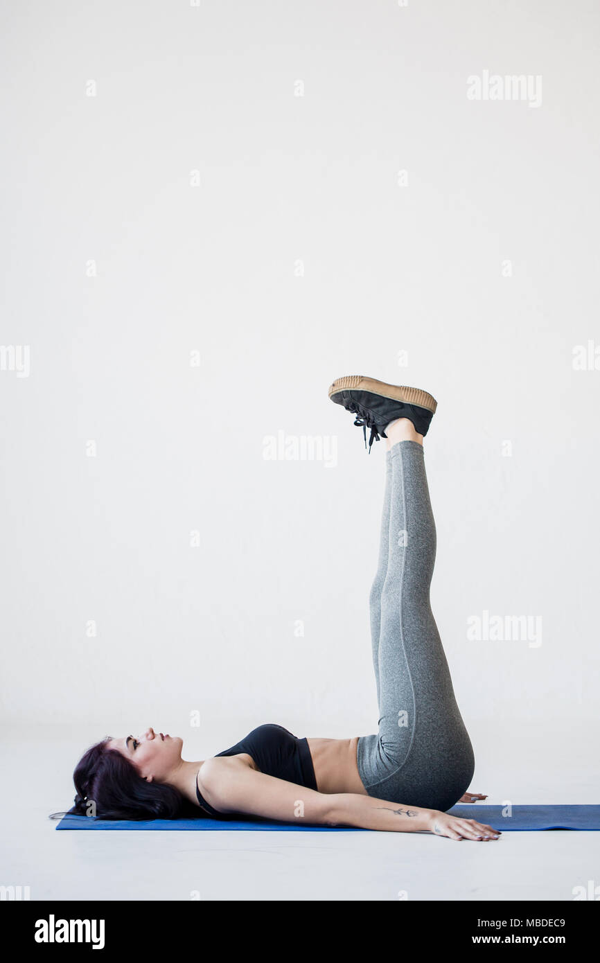 Tutoriels pour débutants sport. La jeune femme est remise en forme allongé sur le tapis et d'élever ses jambes jusqu'à la white studio. Banque D'Images
