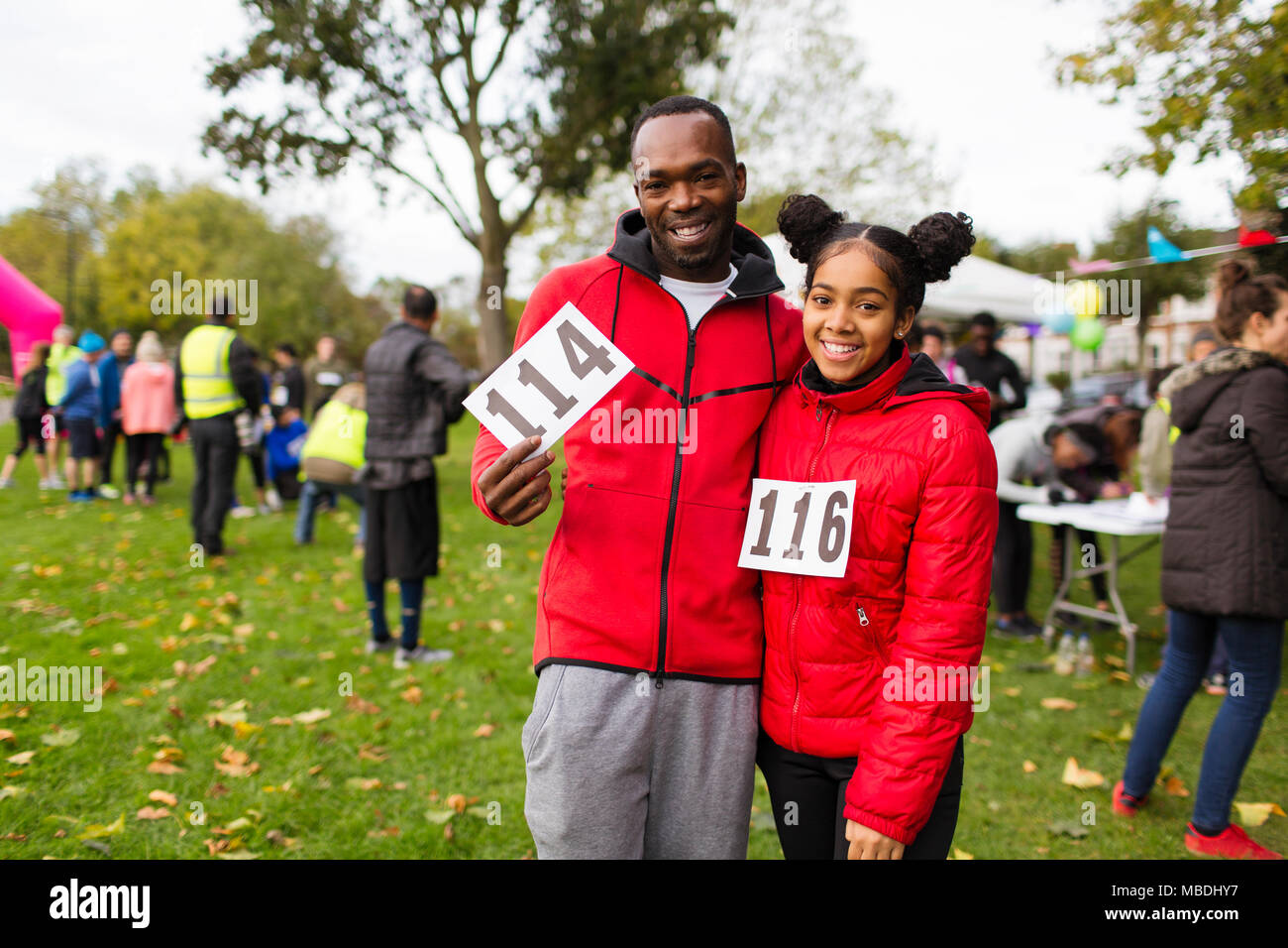 Portrait souriant, confiant père et fille porteur avec marathon bavoirs de charity run dans park Banque D'Images