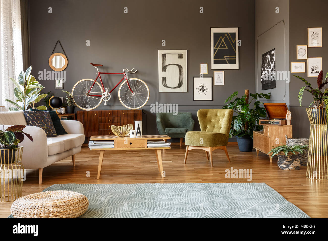 Des affiches sur le mur gris vintage, Fauteuil, Canapé, sol en bois blanc, table et tapis à motifs dans un intérieur salon créatif Banque D'Images