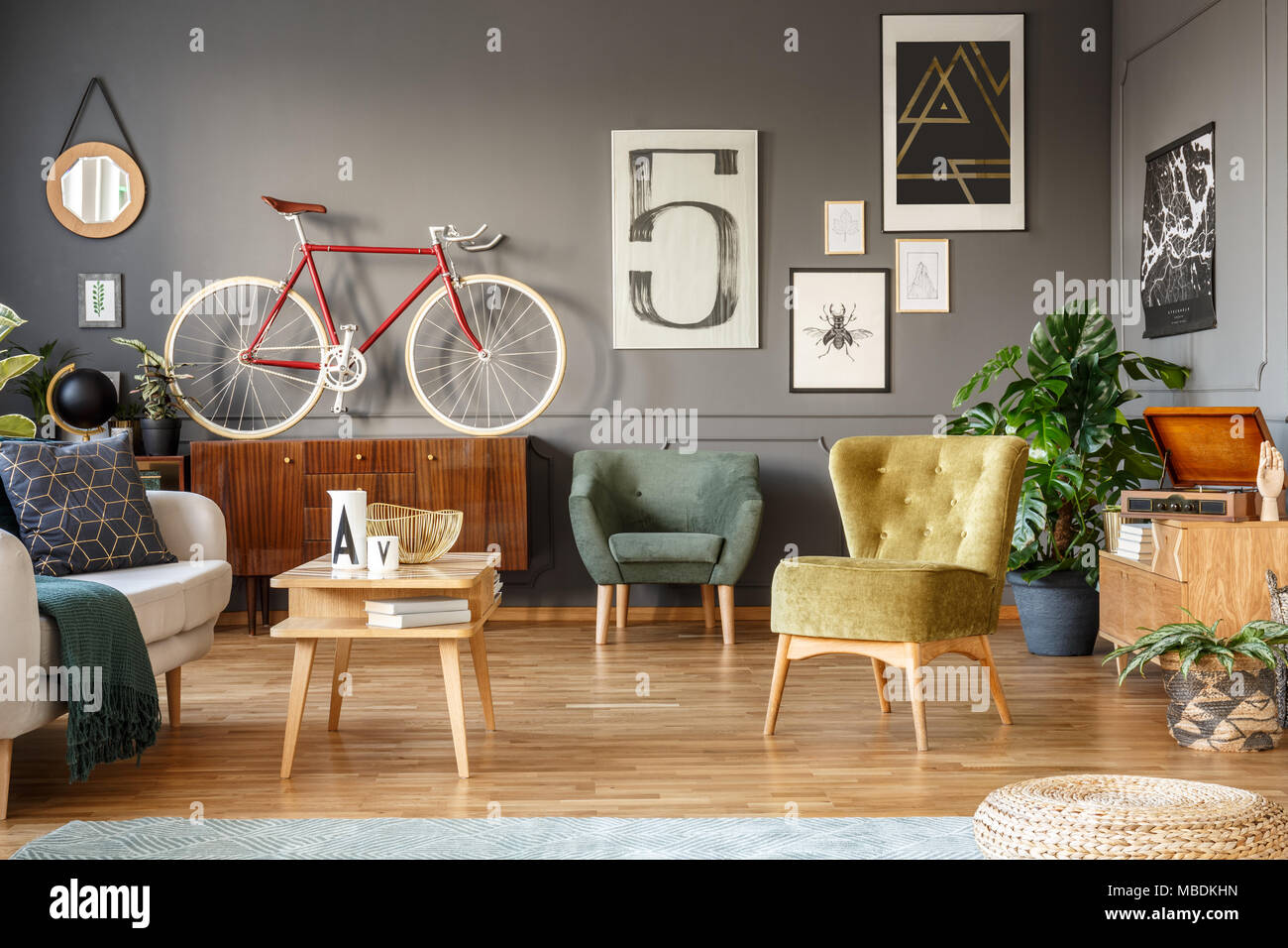 Vélo rouge sur une armoire en bois, fauteuils verts et affiches sur le mur gris dans un salon intérieur Banque D'Images