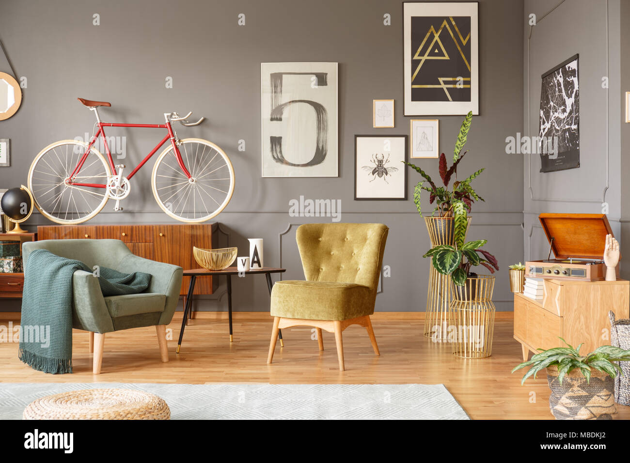 Green fauteuils, table avec un bol d'or, des plantes, des affiches et du vélo dans un salon intérieur Banque D'Images
