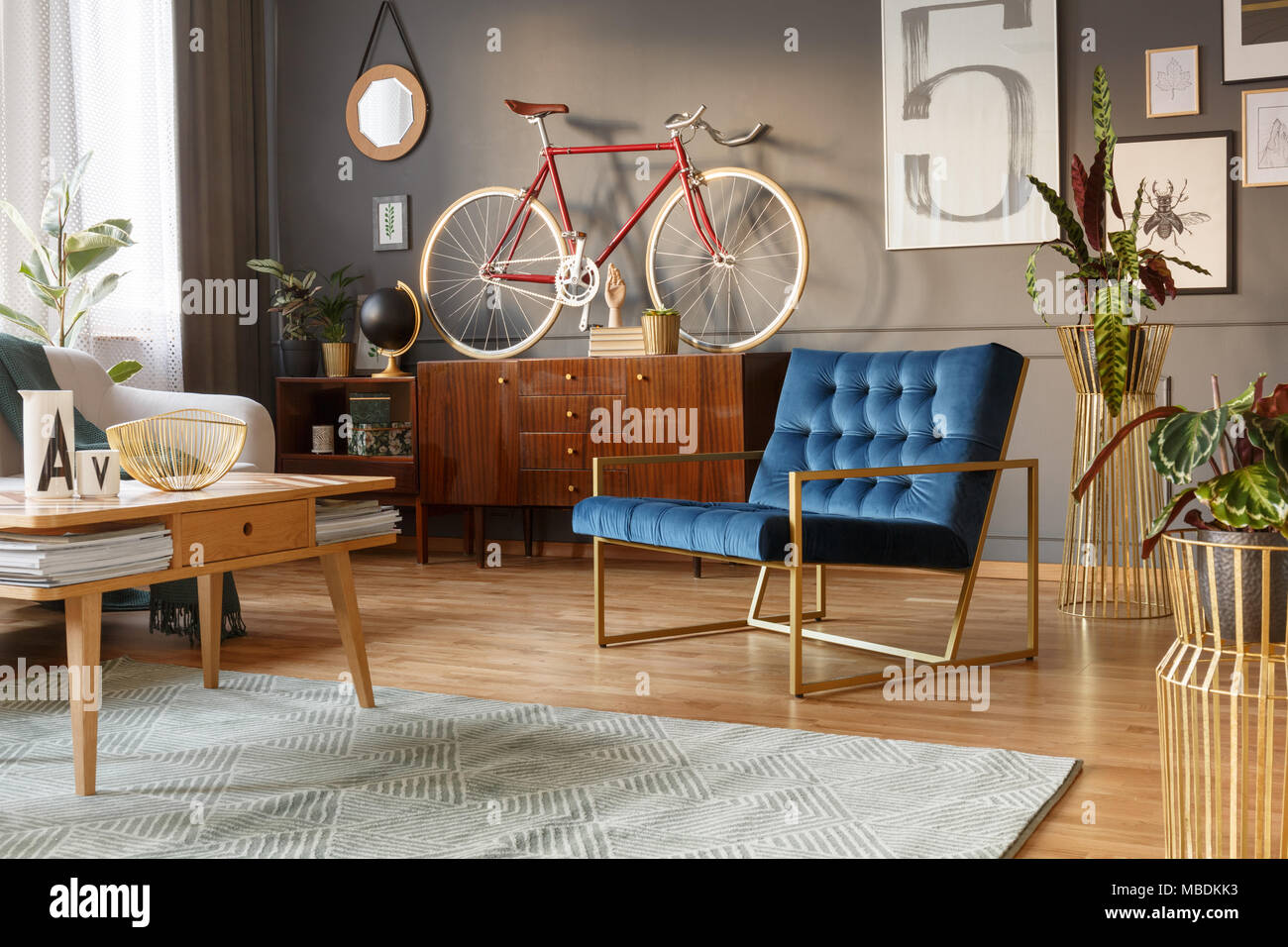 Fauteuil d'or et bleu, table en bois et rétro avec un vélo sur l'armoire en haut d''un salon intérieur Banque D'Images