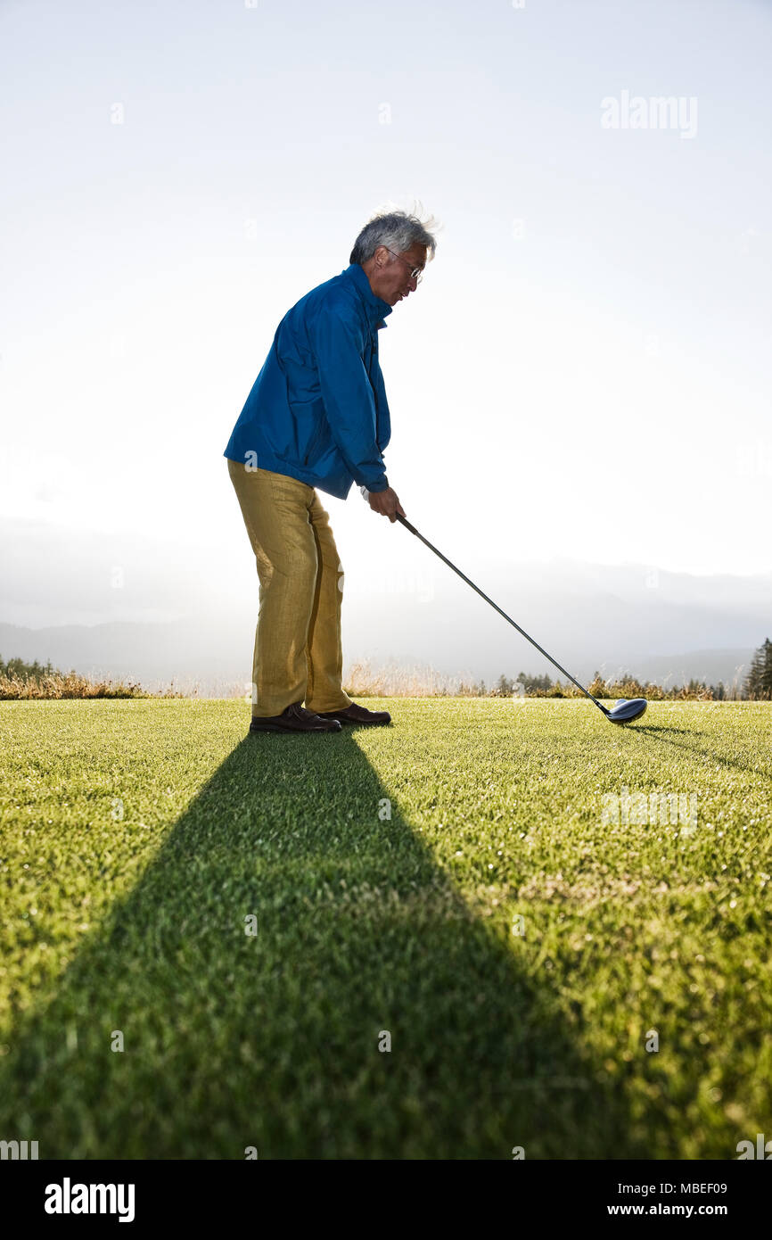 Une asiatique senior man partiront d'une balle de golf et prêt à swing. Banque D'Images